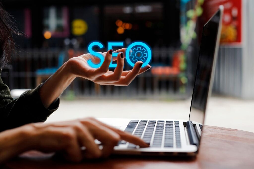 Person drückt eine Taste auf einem Laptop und hält in der anderen Hand den Schriftzug: SEO